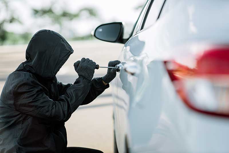 Close-up of an individual attempting to unlock a vehicle door with a screwdriver