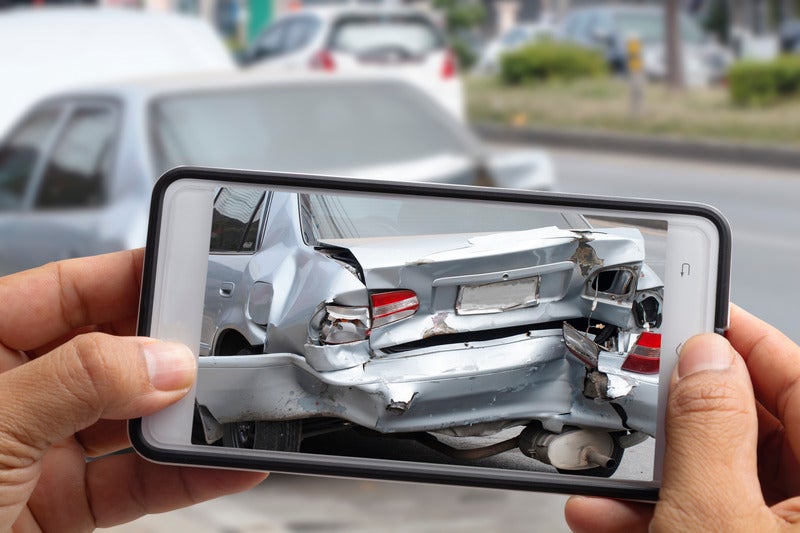Person documenting rear-end vehicle damage with a smartphone after an accident
