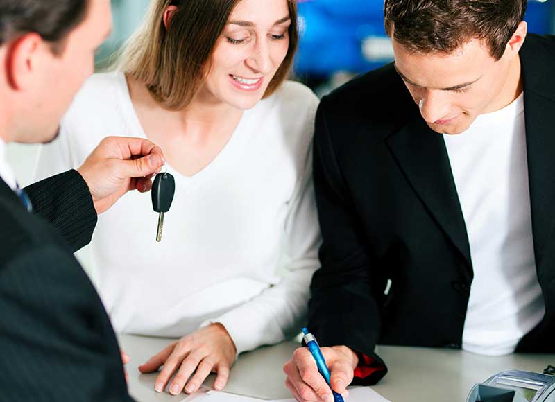 People reviewing and signing vehicle purchase paperwork while receiving car keys