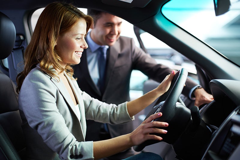Person testing the driver's seat and steering wheel of a vehicle in a dealership showroom