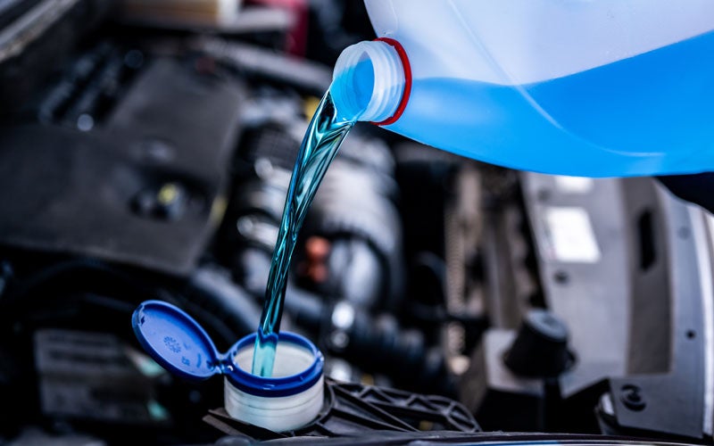 Windshield washer fluid being poured into a vehicle reservoir under the hood